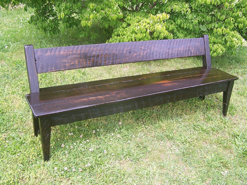 May include: A dark brown wooden bench with a simple design. The bench has a back and is made of reclaimed wood. It is sitting on a grassy lawn.