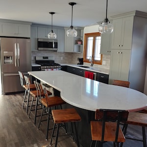 May include: A modern kitchen with gray cabinets, stainless steel appliances, and a large white quartz island with a curved edge. The island has a black base and features several wooden bar stools with black metal frames.