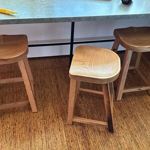 May include: Three wooden bar stools with curved seats and four legs. The stools are made of light-colored wood and have a natural finish. The stools are positioned in front of a countertop.