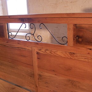 Op de afbeelding: Een houten hoofdbord met een decoratief metalen scrollwerk ontwerp in het midden. Het hoofdbord is gemaakt van gerecycled hout en heeft een rustieke uitstraling.