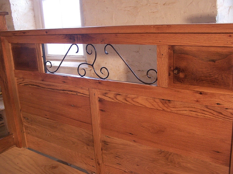 Op de afbeelding: Een houten hoofdbord met een decoratief metalen scrollwerk ontwerp in het midden. Het hoofdbord is gemaakt van gerecycled hout en heeft een rustieke uitstraling.