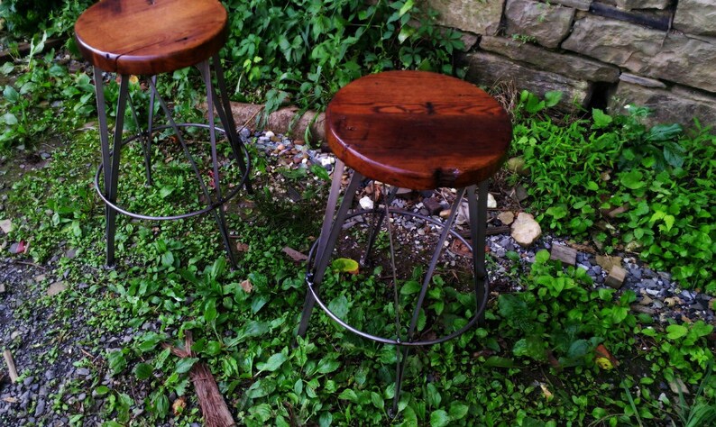 May include: Two rustic wooden stools with metal frames. The stools have a dark brown wood finish and are set on a bed of green grass.