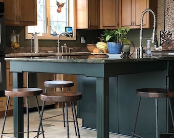 Puede incluir: Una isla de cocina verde oscuro con una encimera de granito y cuatro taburetes de bar de metal negro. La isla tiene una tapa y patas de madera.