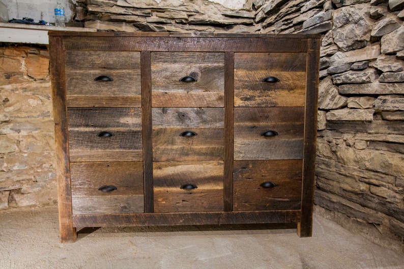 May include: A rustic wooden dresser with nine drawers, each with a black metal knob. The dresser is made of reclaimed wood and has a natural, weathered finish.