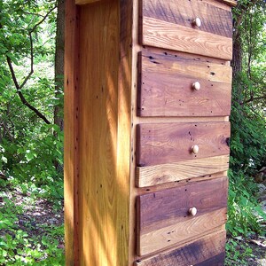 May include: A tall wooden chest of drawers with five drawers. The chest is made of reclaimed wood and has a rustic, farmhouse style. The drawers have simple wooden knobs.