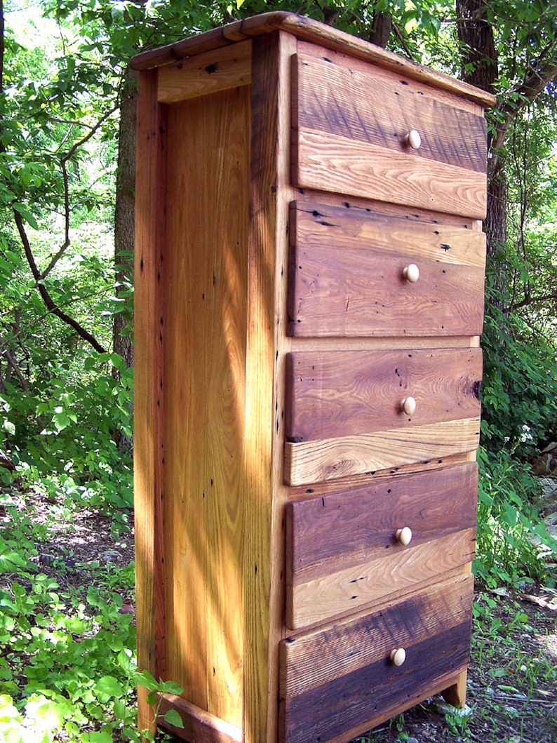 May include: A tall wooden chest of drawers with five drawers. The chest is made of reclaimed wood and has a rustic, farmhouse style. The drawers have simple wooden knobs.