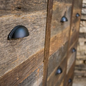 May include: A rustic wooden dresser with black metal drawer pulls. The dresser is made of reclaimed wood and has a natural, weathered finish.