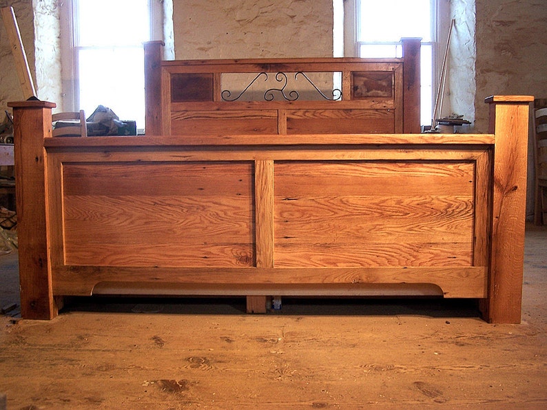 Op de afbeelding: Een houten bedframe met een hoofdbord met een decoratief metalen scroll-ontwerp. Het frame is gemaakt van gerecycled hout met een natuurlijke afwerking.