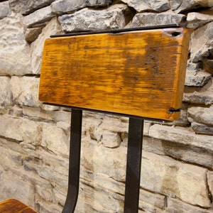 May include: A rustic wooden chair with a metal frame. The chair has a simple design with a wide, flat seat and a back that is slightly angled. The wood is a rich brown color and has a natural, weathered finish. The metal frame is black and has a slightly industrial look.