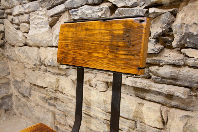 May include: A rustic wooden chair with a metal frame. The chair has a simple design with a wide, flat seat and a back that is slightly angled. The wood is a rich brown color and has a natural, weathered finish. The metal frame is black and has a slightly industrial look.