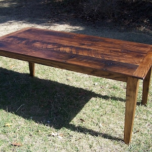 May include: A rustic wooden table with a dark brown finish. The table has a rectangular top and four legs. The table is made of reclaimed wood and has a distressed look.