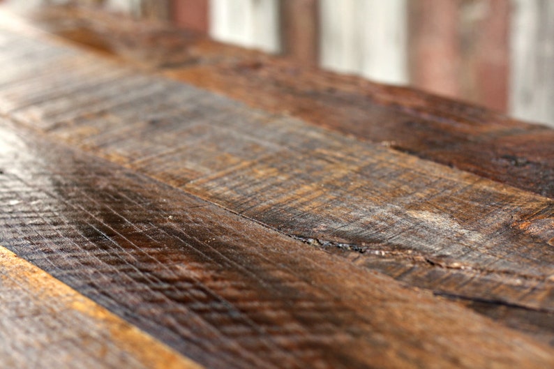 May include: Close-up of a rustic wooden table top with a natural wood grain pattern. The wood is a mix of brown and dark brown shades, with a few knots and imperfections.