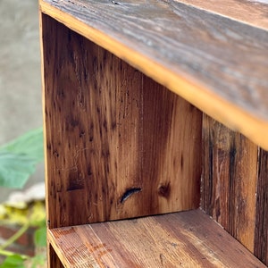 May include: Close-up of a rustic wooden shelf unit. The unit is constructed from reclaimed wood, showcasing a mix of light and dark brown tones with visible wood grain and knots. The design features a simple, open-shelf structure, perfect for displaying items.