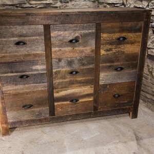 May include: A rustic wooden dresser with nine drawers and black metal drawer pulls. The dresser is made of reclaimed wood and has a natural, weathered finish.