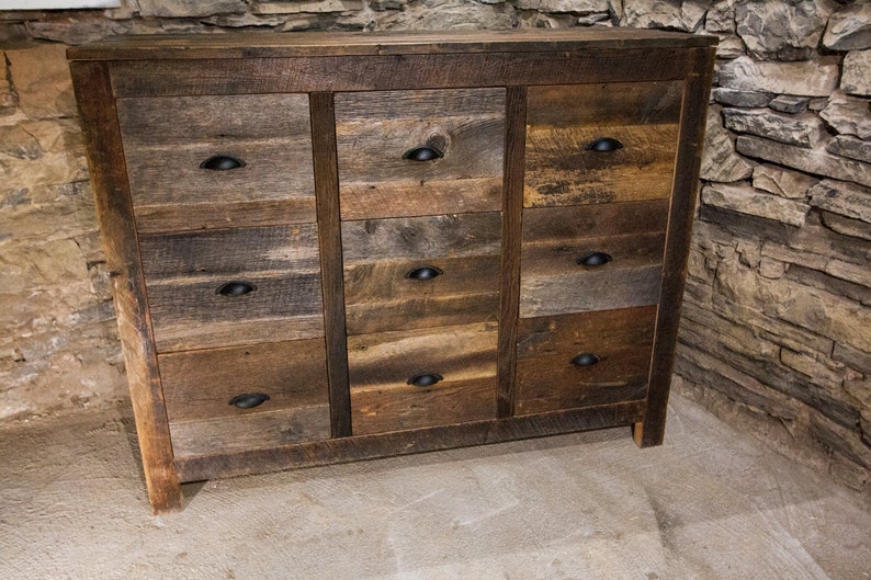 May include: A rustic wooden dresser with nine drawers and black metal drawer pulls. The dresser is made of reclaimed wood and has a natural, weathered finish.