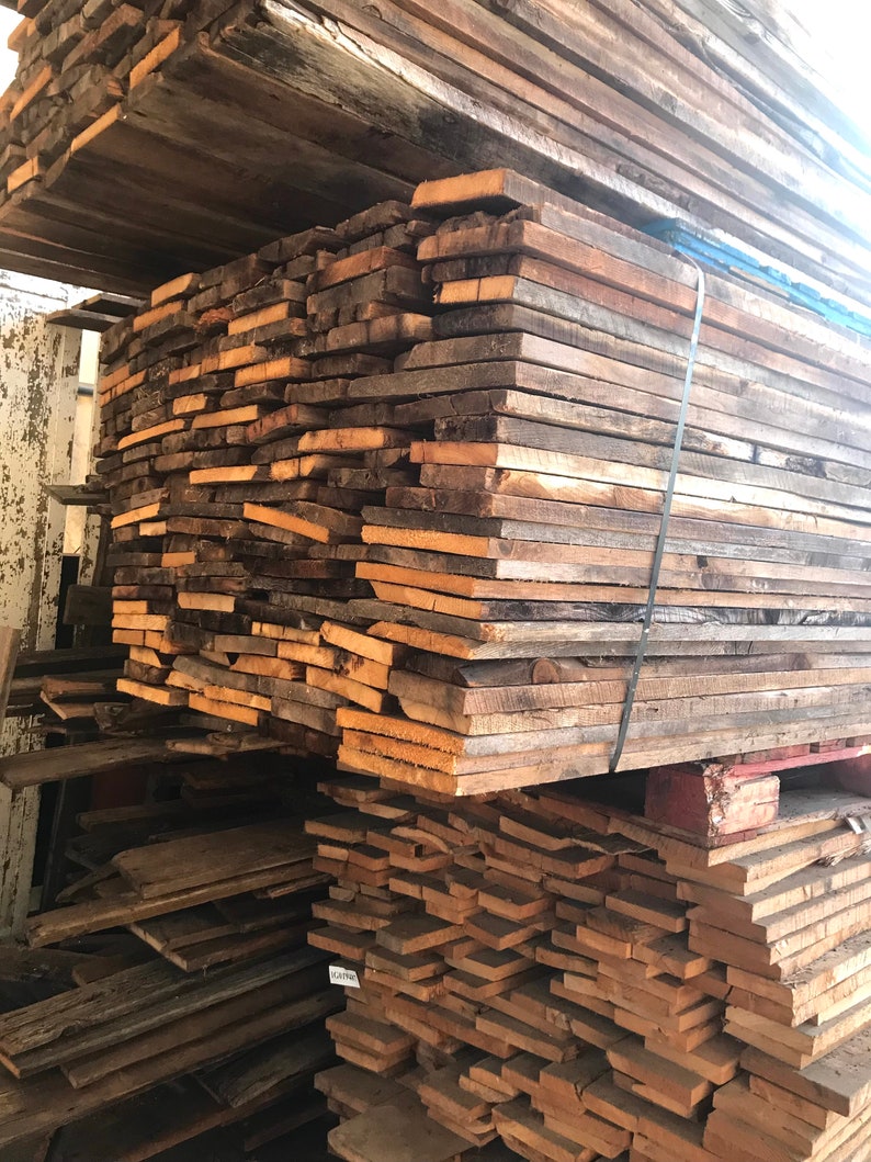 May include: A large stack of reclaimed wood planks, varying in shades of brown and tan. The wood appears weathered and aged, with visible grain and texture. The planks are bundled together, suggesting they are ready for use in a woodworking project or construction.