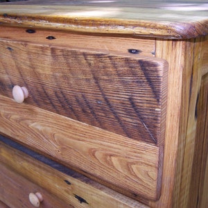 May include: A wooden dresser with three drawers and a light brown stain. The drawers have simple wooden knobs. The dresser is made of reclaimed wood with a rustic look.