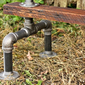 May include: A rustic wooden bench with black metal pipe legs. The bench is made from reclaimed wood and has a natural finish. The pipe legs are attached to the bench with flanges.