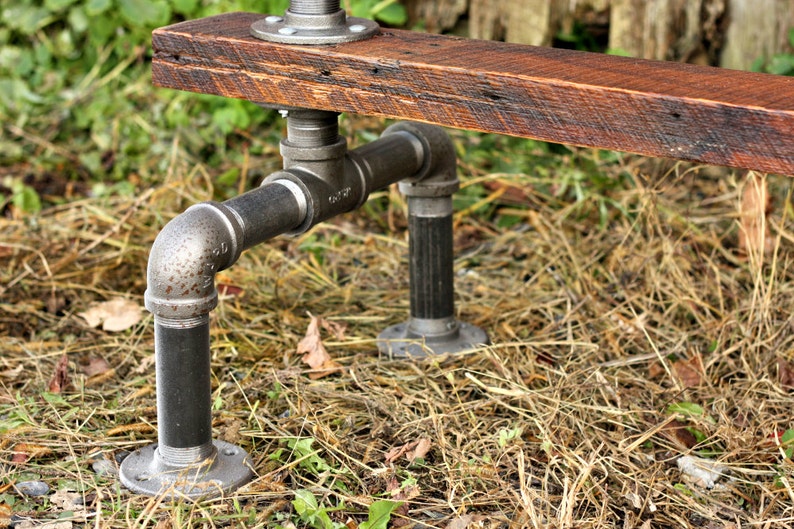 May include: A rustic wooden bench with black metal pipe legs. The bench is made from reclaimed wood and has a natural finish. The pipe legs are attached to the bench with flanges.