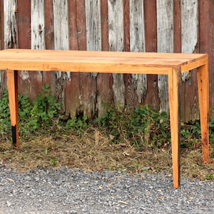 May include: A rustic wooden table with a natural wood finish and black painted legs. The table is made of reclaimed wood and has a simple, modern design.