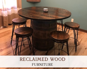 Puede incluir: Una mesa de madera reciclada con una base de barril y cuatro taburetes a juego. La mesa y los taburetes tienen un acabado de madera marrón oscuro. La mesa es redonda y tiene un diámetro de aproximadamente 120 cm. Los taburetes tienen un marco de metal y un asiento redondo.