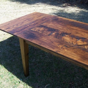 May include: A rustic wooden table with a dark brown stain. The table top is made of reclaimed wood planks with a knotty grain pattern. The table has a single visible leg made of solid wood.