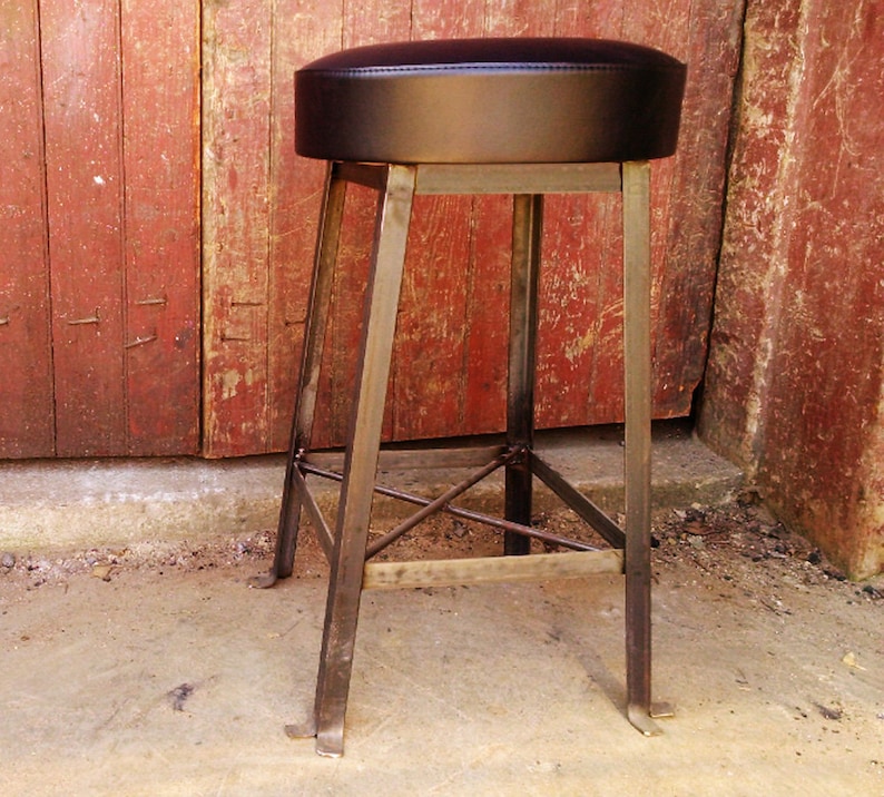 Puede incluir: Un taburete de bar de metal negro con un asiento de cuero negro. El taburete tiene un dise&ntilde;o simple e industrial con una estructura de metal resistente.
