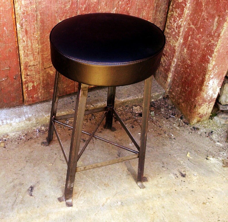 Puede incluir: Un taburete de metal con un asiento de cuero negro. El taburete tiene un dise&ntilde;o sencillo con un asiento redondo y cuatro patas.