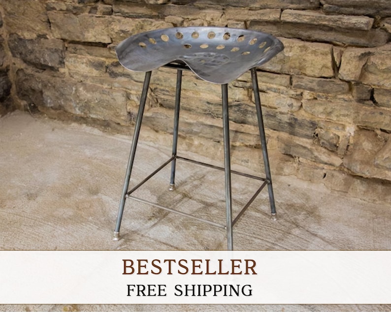 May include: A metal stool with a unique seat made from a repurposed tractor seat. The seat has a distinctive pattern of holes and a slightly curved shape. The stool has a simple, industrial design with four legs and a crossbar for support.