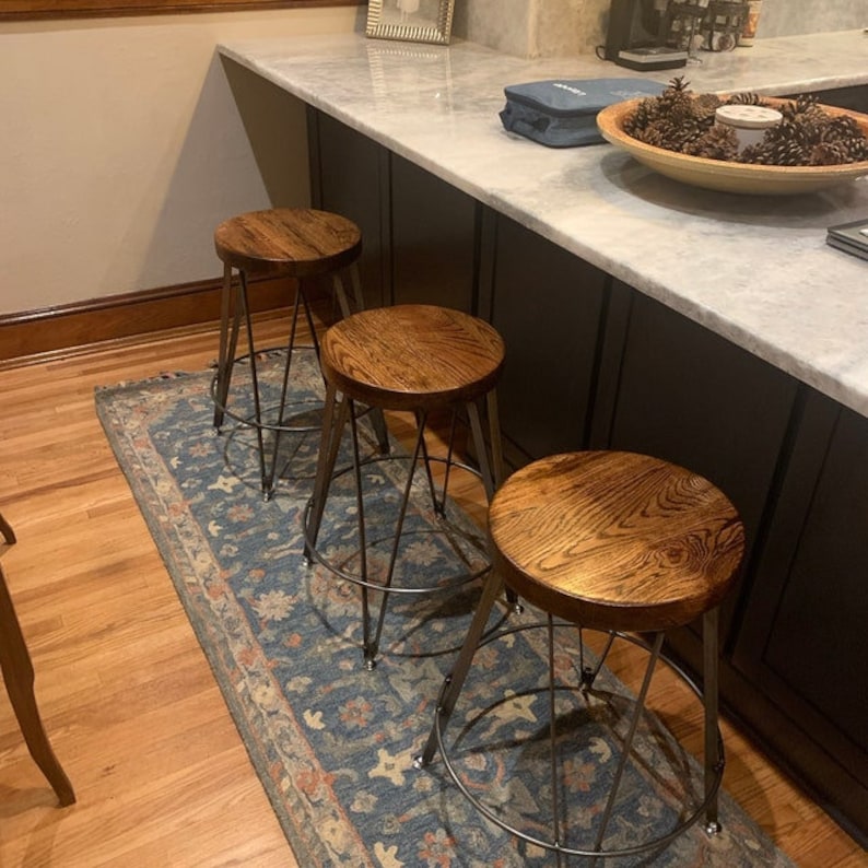 May include: Three wooden bar stools with black metal frames. The stools are arranged in a row on a blue and brown patterned rug. The stools have a dark wood finish and a simple design.