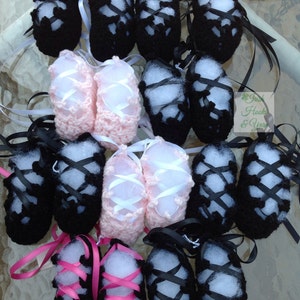 Op de afbeelding: Een verzameling gehaakte babyschoentjes in zwart en roze. De schoentjes hebben witte lintjes en zijn gebonden in een strik. De schoentjes zijn in een groep op een tafel gelegd.