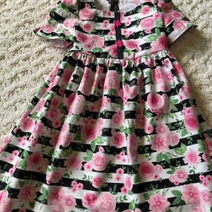 May include: A black and white striped dress with a pink floral pattern. The dress has short sleeves and a round neckline. It has a zipper closure in the back and a button closure at the top.