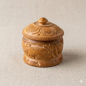 May include: A small, round wooden box with a lid. The box and lid are carved with floral and geometric patterns. The box is light brown in color and appears to be made of wood. The lid has a small knob on top.