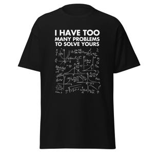 Peut inclure: T-shirt noir avec le texte blanc : "I HAVE TOO MANY PROBLEMS TO SOLVE YOURS." Le t-shirt présente un motif de formules mathématiques complexes en blanc. Un tee-shirt décontracté et confortable.