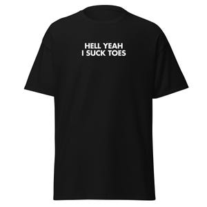 Può includere: T-shirt nero con la scritta bianca "HELL YEAH I SUCK TOES" stampata sul petto. Il testo è in grassetto e in un carattere sans-serif. La t-shirt è un classico girocollo, realizzata in tessuto morbido.