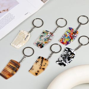 May include: A collection of comb-shaped keychains in various colors and patterns. Some keychains have names like "Sarah" and "Becca" printed on them. The keychains are attached to silver key rings.
