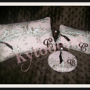May include: Three pink and brown quilted zippered pouches with a toile pattern. The pouches are monogrammed with the letter "C" in brown thread. The pouches are on a brown fabric surface.