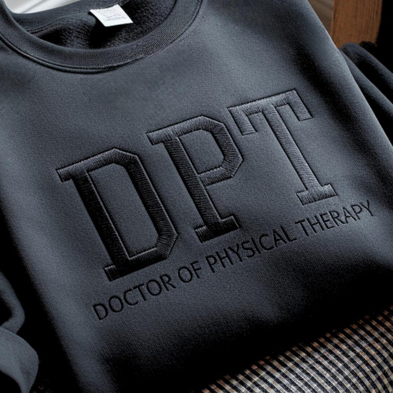 May include: Dark gray sweatshirt with the embroidered letters "DPT" above the words "DOCTOR OF PHYSICAL THERAPY". The sweatshirt is made of a soft material and has a crew neck.