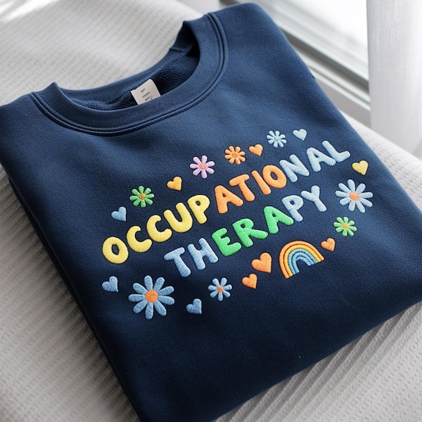 Può includere: Una felpa girocollo blu navy con il testo ricamato OCCUPATIONAL THERAPY in lettere multicolori. Il design è circondato da piccole icone ricamate tra cui vari fiori colorati, cuori e un piccolo arcobaleno.