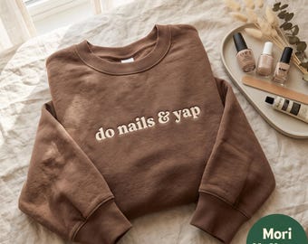 Puede incluir: Una sudadera marrón de cuello redondo con el texto "do nails & yap" bordado en hilo de color crema en el pecho. La prenda tiene mangas largas con puños acanalados y un cuello acanalado, confeccionada con una tela de color sólido.