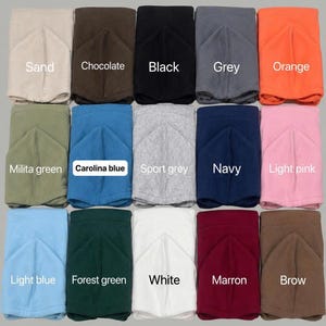 May include: A hoodie color chart displaying fifteen folded hoodies in various colors including sand, chocolate, black, grey, orange, military green, Carolina blue, sport grey, navy, light pink, light blue, forest green, white, maroon, and brown.