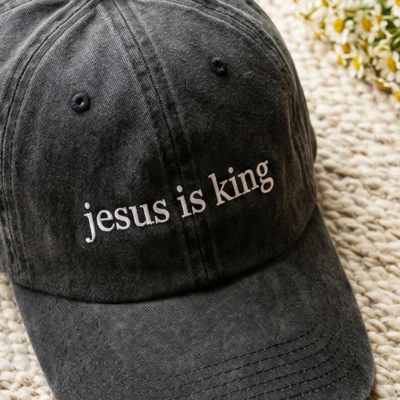May include: A charcoal gray baseball cap with the embroidered text "jesus is king" in white. The cap has a curved brim and a classic six-panel design. The hat is made of a soft, worn fabric.