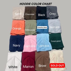 May include: A hoodie color chart displaying sixteen folded hooded sweatshirts in various colors including sand, chocolate, black, grey, orange, military green, Carolina blue, sport grey, navy, light pink, light blue, forest green, white, maroon, and brown.