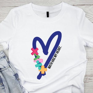 Op de afbeelding: Wit T-shirt met een blauw hartontwerp en de tekst "Math has my heart." Het hart is versierd met kleurrijke wiskundige symbolen.