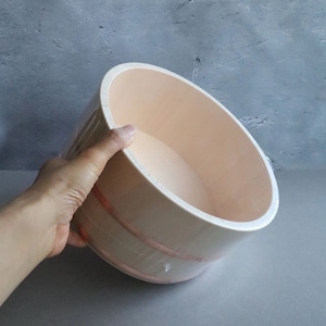 Traditional Japanese hinoki wood bath bucket with copper bands, elegantly placed on a stone ledge surrounded by lush greenery, evoking an authentic onsen experience.