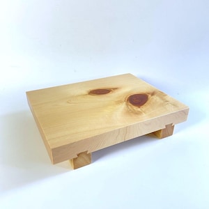 May include: A natural wood serving tray with a light brown finish and a raised edge. The tray has four small legs and is made of solid wood.