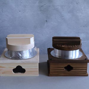 Może przedstawiać: Dwa drewniane parowary do ryżu z metalowymi wkładami. Parowar po lewej stronie jest wykonany z jasnego drewna i ma naturalne wykończenie. Parowar po prawej stronie jest wykonany z ciemnego drewna i ma brązowe wybarwienie.