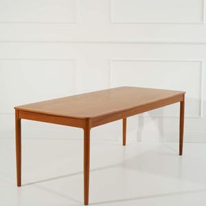Könnte beinhalten: Ein rechteckiger Esstisch aus Holz mit einer hellbraunen Oberfläche und vier schlanken Beinen. Der Tisch ist aus massivem Holz gefertigt und hat ein schlichtes, elegantes Design.