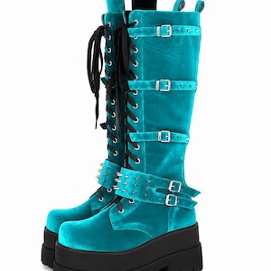 May include: Turquoise velvet knee-high boots with black platform soles. The boots feature multiple silver buckles, studded accents, and black laces. The platform sole measures approximately 3 inches.