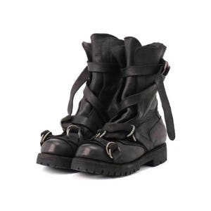 May include: A pair of black leather boots with multiple straps and silver-tone metal rings. The boots have a rugged, distressed appearance and a thick sole. The design features a combination of buckles and straps for closure and detail.